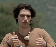 a young man wearing a brown shirt giving the thumbs up sign