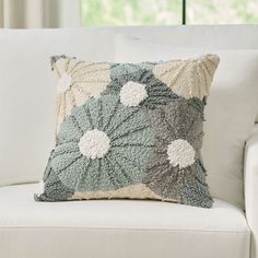 a white couch with a decorative pillow on it's back and windows in the background