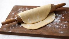 a wooden cutting board topped with dough and a rolling pin