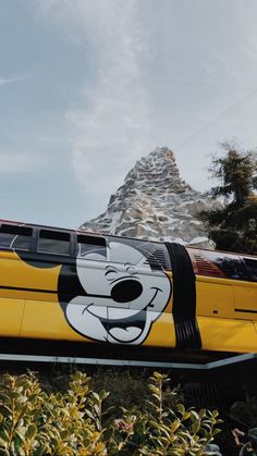 a yellow train with mickey mouse painted on it's side and mountains in the background