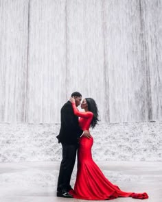 a man and woman standing next to each other in front of a waterfall with their arms around each other