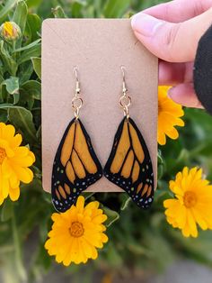 a pair of yellow and black butterfly wings hanging from dangle earrings in front of flowers