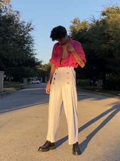 a woman standing on the side of a road wearing white pants and a pink shirt