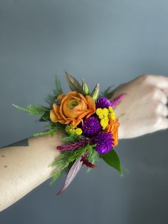 a woman's arm holding a bouquet of flowers and greenery in her left hand