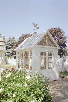 a small white house with a chicken on top of it's roof and windows