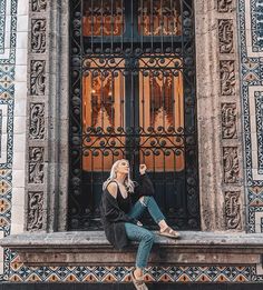 a woman sitting on a ledge in front of an ornate building with wrought iron doors