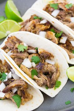 three shredded pork tacos on a plate with limes and cilantro wedges