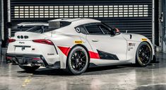 a white sports car parked in front of a garage door with red and yellow stripes