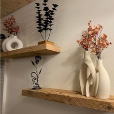 three white vases are sitting on wooden shelves with decorative decorations in the corner behind them