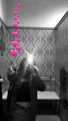 a woman taking a selfie in a bathroom with pink hearts hanging from the ceiling