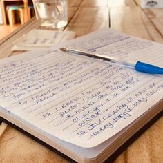 a notepad with writing on it and a pen sitting on top of it next to a glass of water