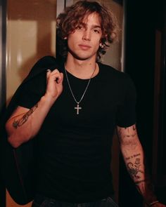 a young man with tattoos and a cross on his chest is standing in front of a door