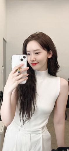 a woman taking a selfie in front of a mirror wearing a white dress and holding a cell phone