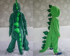 two children in green dinosaur onesuits standing next to each other on a bed