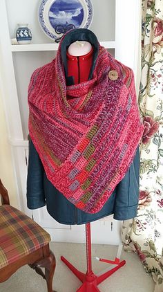 a red knitted shawl sitting on top of a mannequin next to a window