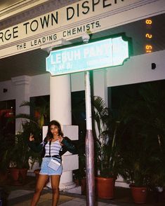 a woman standing next to a street sign in front of a building with palm trees