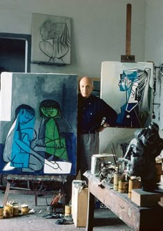 an older man standing in front of some art work on easels and canvass