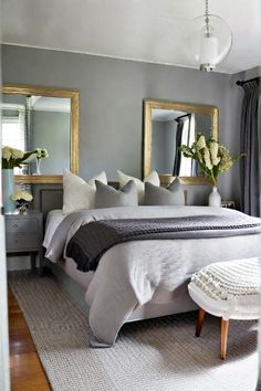 a large bed sitting in a bedroom next to two mirrors and a table with flowers on it