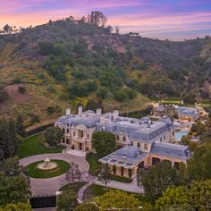 an aerial view of a mansion in the hills with trees and bushes surrounding it at sunset