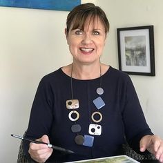 a woman sitting at a table holding a paintbrush and painting an image on a piece of paper