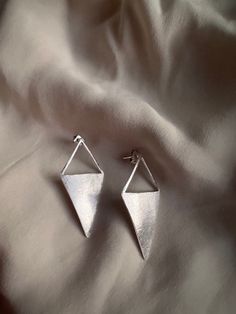 two silver earrings sitting on top of a white cloth covered bed sheet with the fabric behind them