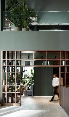 a woman walking through a room with lots of bookshelves and potted plants