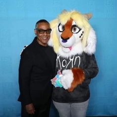 a man standing next to a mascot in front of a blue wall