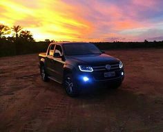 a black truck parked on top of a dirt field under a colorful sky at sunset