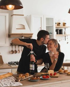 a man and woman sitting at a kitchen counter drinking wine