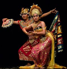 two people dressed in costumes and headdress, one holding a fan while the other holds