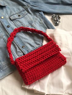 a crocheted red purse sitting on top of a white shirt next to a denim jacket