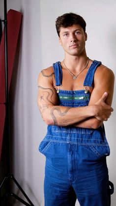 a man with his arms crossed wearing overalls