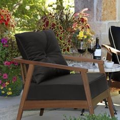 two chairs and a table on a patio with flowers in the back ground, next to each other