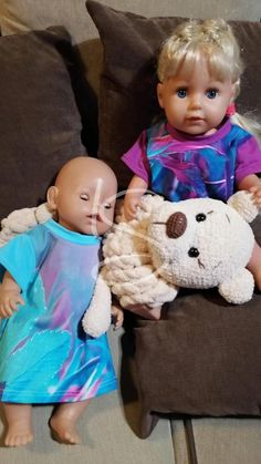 two dolls sitting next to each other on top of a couch, one holding a stuffed animal