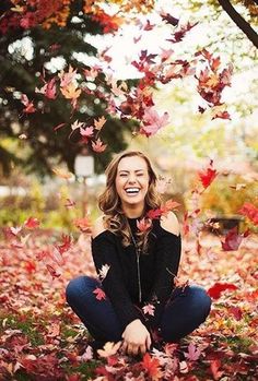 a woman sitting on the ground surrounded by leaves and smiling at the camera with her eyes closed