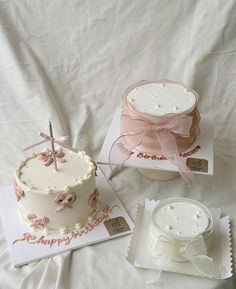 two small cakes are sitting next to each other on a bed with white sheets and pink bows