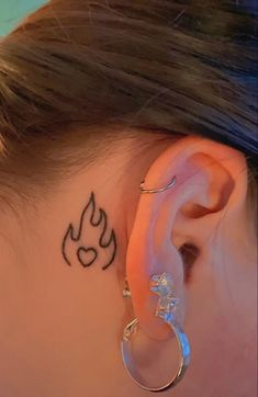 a woman with a tattoo on her ear and behind the ear is a pair of hoop earrings