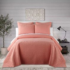 a bed with pink comforter and pillows in a room next to a lamp on a table