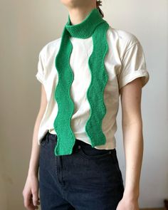 a woman wearing a green knitted scarf and white t - shirt with her hands in her pockets