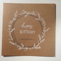 a brown card with the words happy birthday written in white on it and a wreath