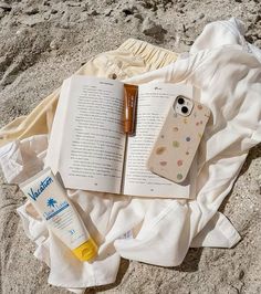 an open book sitting on top of a sandy beach next to a bottle of sunscreen