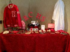 a red table topped with lots of personal items and pictures next to a baseball jacket