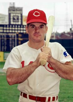 a man holding a baseball bat on top of a field in front of a stadium