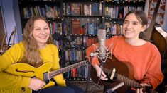 two women sitting in front of a microphone with guitars