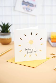 a card with the words sending you sunshine on it sitting on a table next to a potted plant