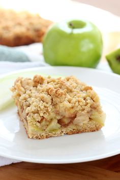 a piece of apple crumb cake on a plate with an apple in the background