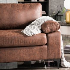 a brown leather couch with a white and black striped blanket on it's back