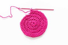 a pink crochet potholder with a hook on the end and a white background