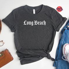 "Presenting our Gothic Long Beach Shirt, a unique and stylish addition to your wardrobe. This Long Beach Graphic Tee is a must-have for anyone who loves the combination of gothic aesthetics and the vibrant spirit of Long Beach. The shirt features intricate Gothic Lettering spelling out \"Long Beach\", making it a standout piece. Designed and printed locally, this Long Beach Local shirt is a true representation of the city's creative spirit. The graphic t-shirt is made from high-quality materials, ensuring comfort and durability. Whether you're a Long Beach local yourself or just a fan of the city's unique vibe, this Gothic Long Beach shirt is a perfect choice. It's more than just a shirt; it's a piece of wearable art that showcases your love for Long Beach and gothic style. PRODUCTION TIME Beachy Relaxed Fit Shirt For Vacation, Beachy Letter Print Shirt For Vacation, Beachy Relaxed Fit Shirt With Letter Print, Relaxed Fit Shirt With Letter Print For Beach Season, Casual Relaxed Fit Shirt For Beach Party, Casual Shirt With Letter Print For Beach Party, Casual Letter Print Shirt For Beach Party, Gothic Letters, Recovery Shirts