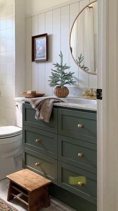 a bathroom with green cabinets and a white toilet next to a wooden step stool in front of the sink